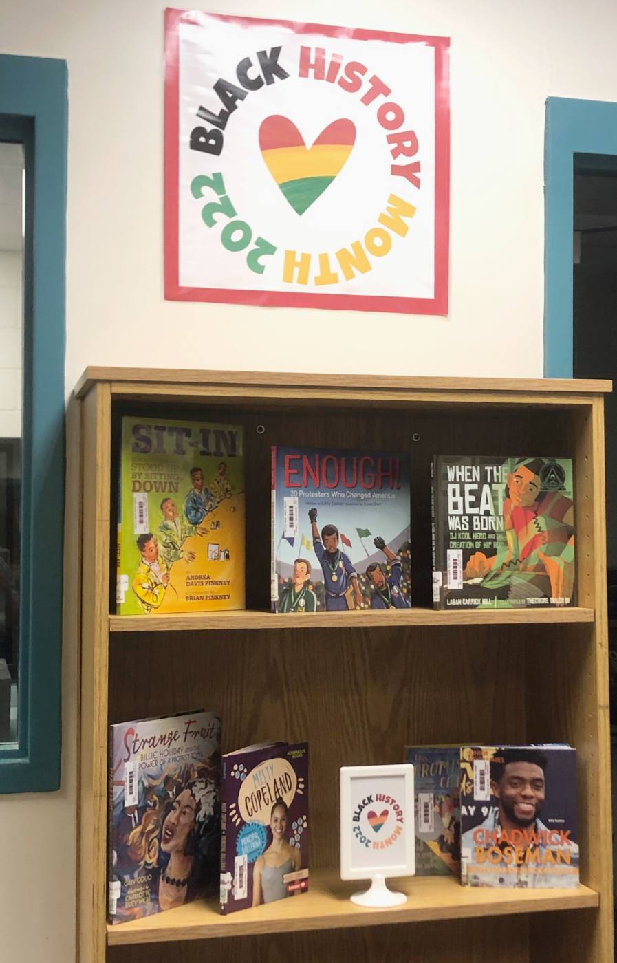 A Black History Month 2022 poster with a striped heart above a shelf of face-out books, with a smaller framed version of the sign on the shelf.