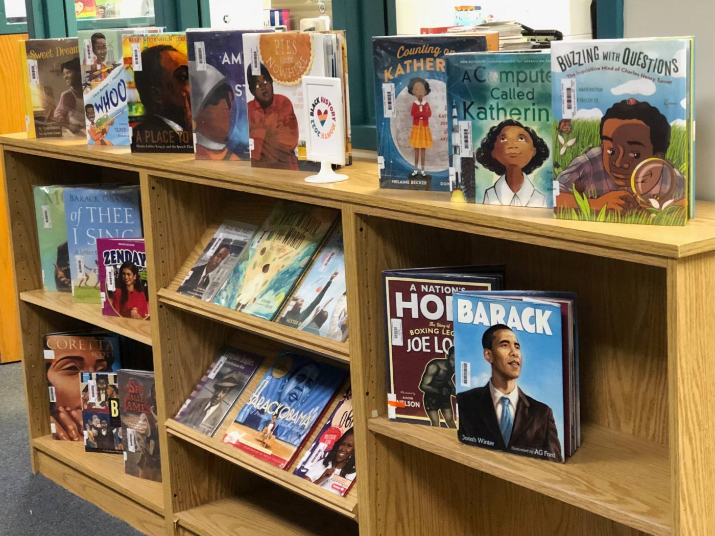 Picture-book biographies displayed face-out along a low shelf, with a framed Black History Month sign among them.