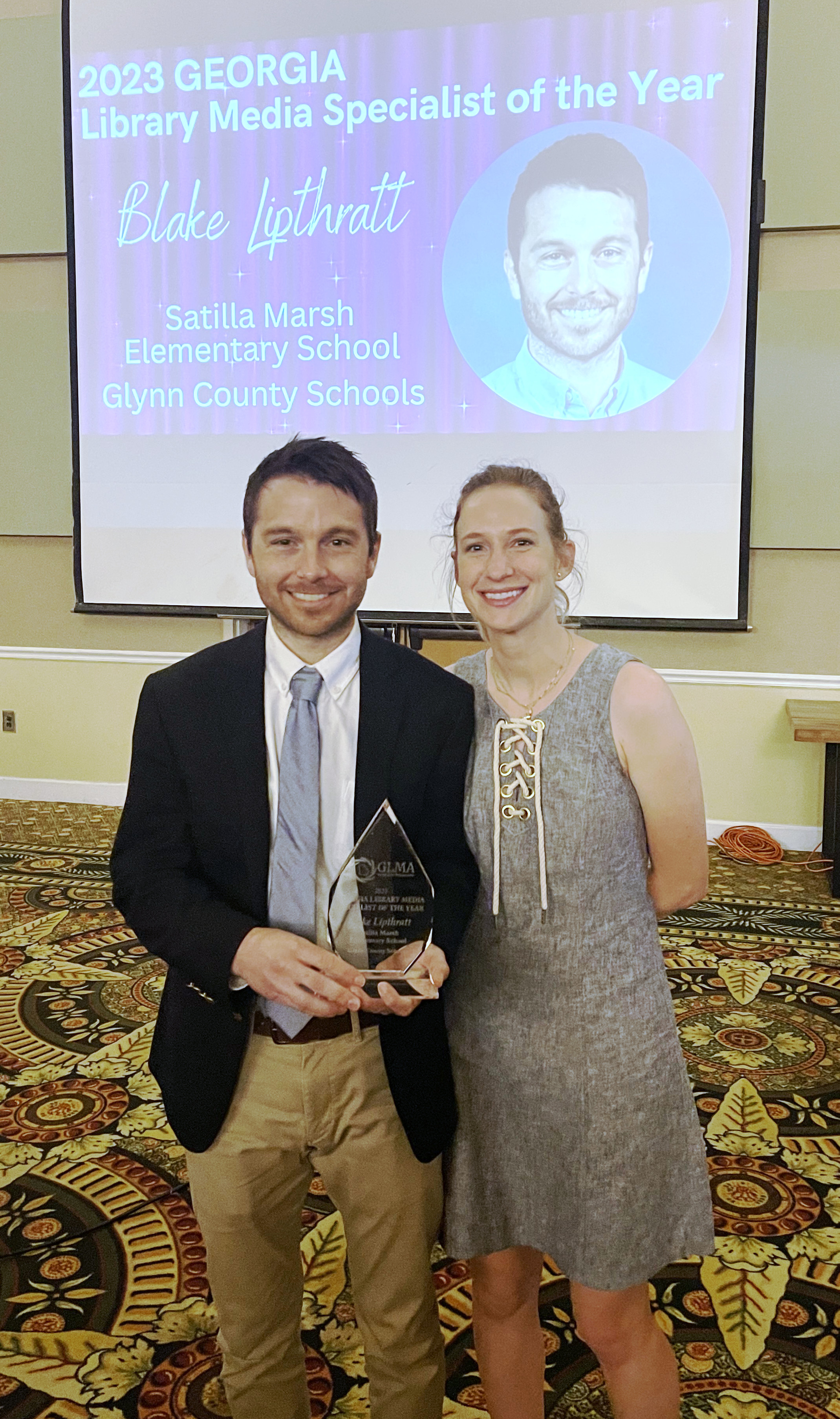 Holding the 2023 Georgia Library Media Specialist of the Year award, standing beside my wife in front of a screen announcing the honor.