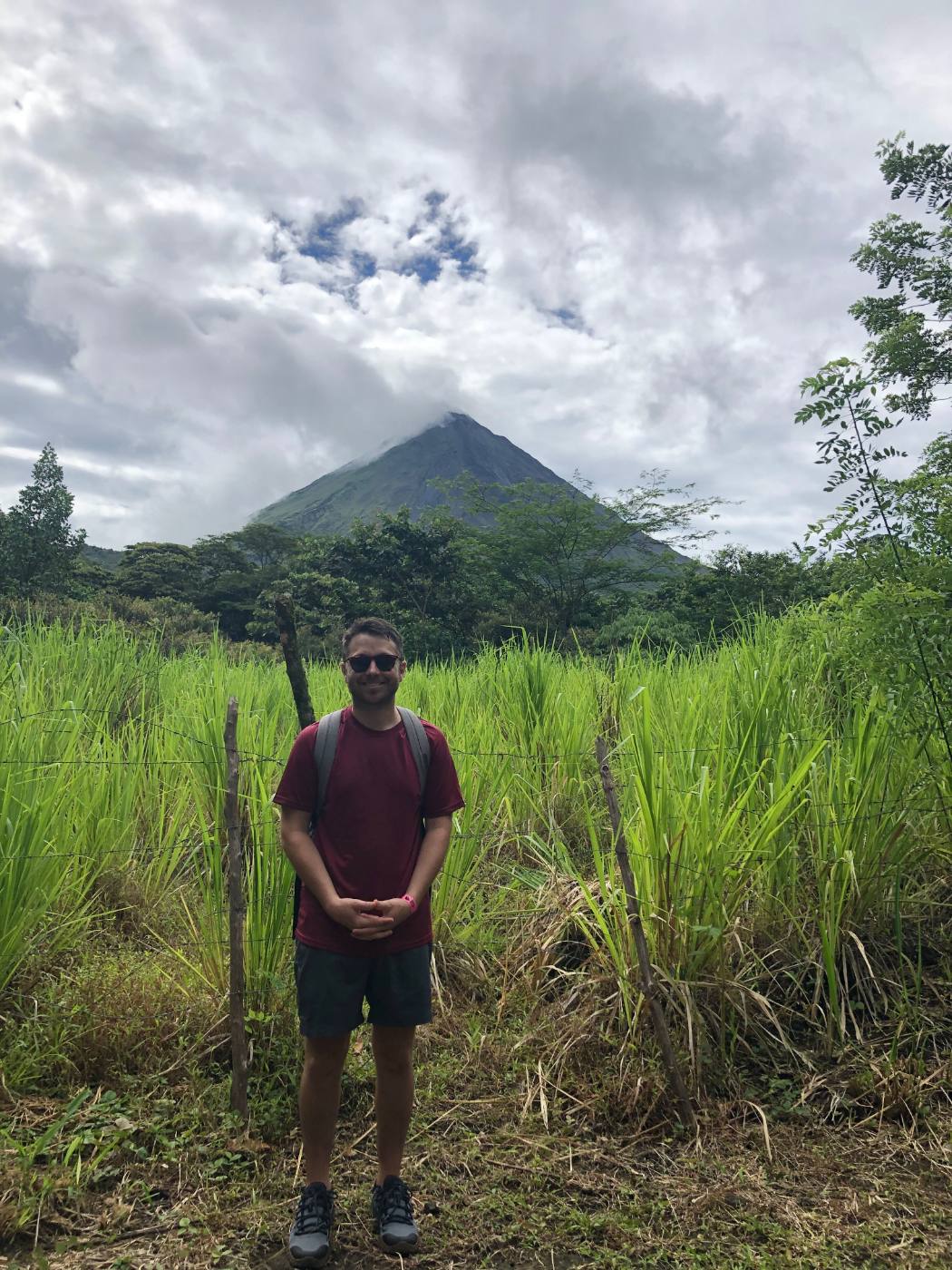 Standing in tall grass in front of Arenal Volcano in Costa Rica, its peak in cloud.