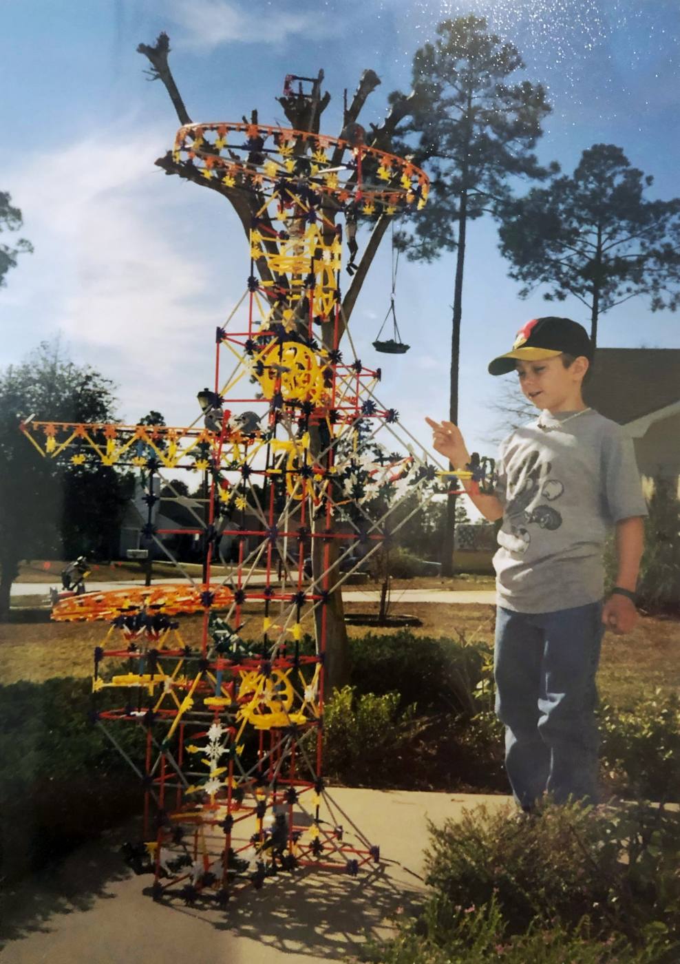 Me at age nine in a ball cap, pointing at a K’NEX tower I built that was taller than I was.