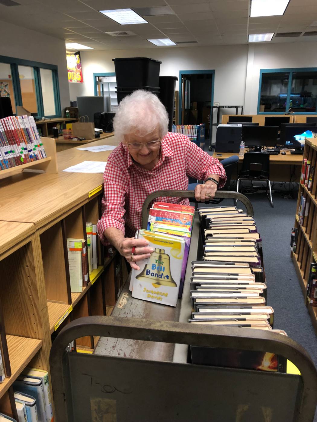 My grandmother, in a red gingham shirt, working through a cart of chapter books with the genre list beside her.