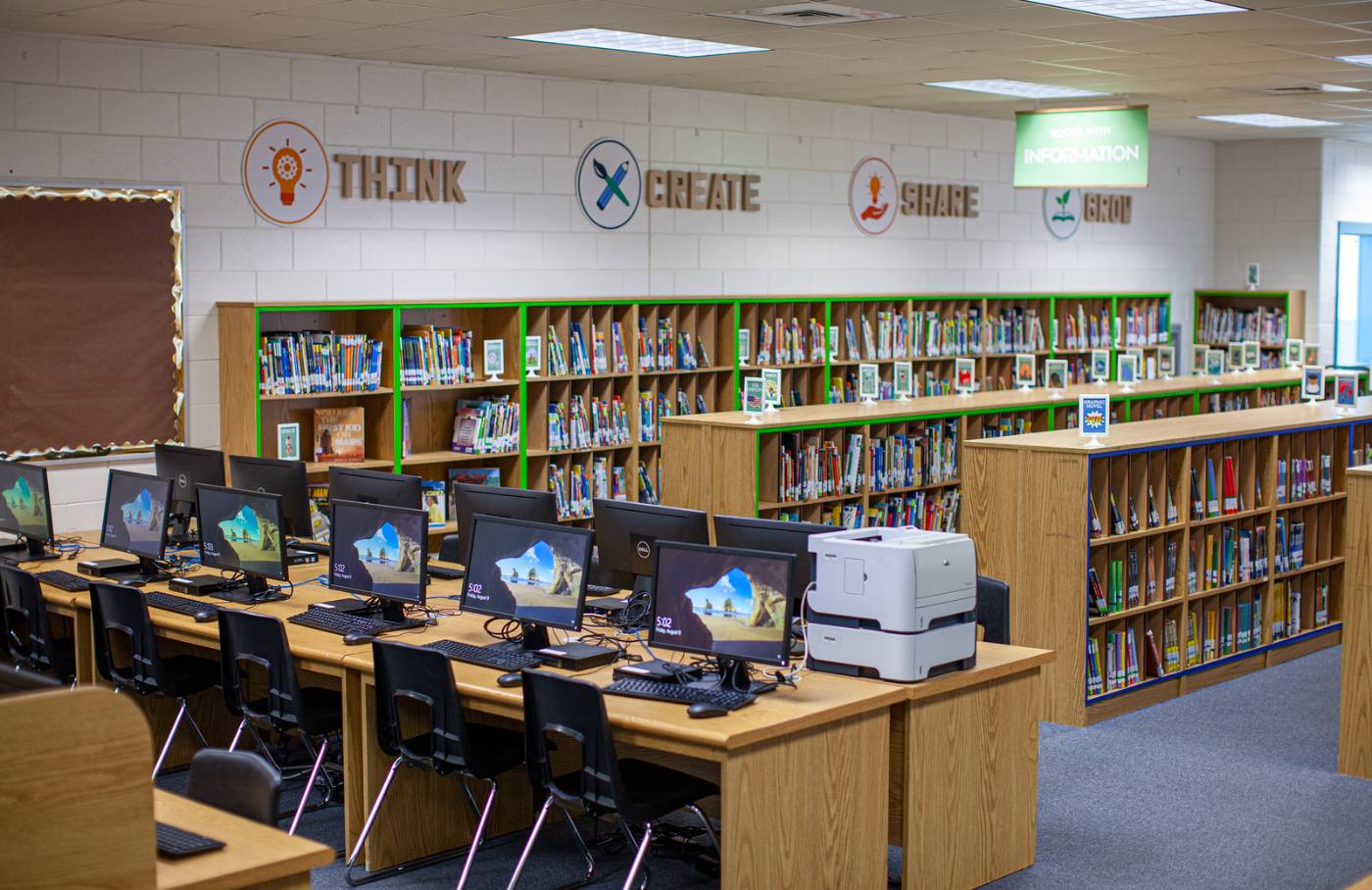 Computer stations in front of green-edged information shelving, with THINK, CREATE, SHARE, GROW lettered across the wall above.