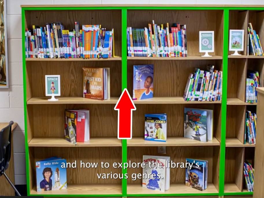 A still from the library orientation video: a red arrow points to a green-edged shelf of space books with a framed Space sign.