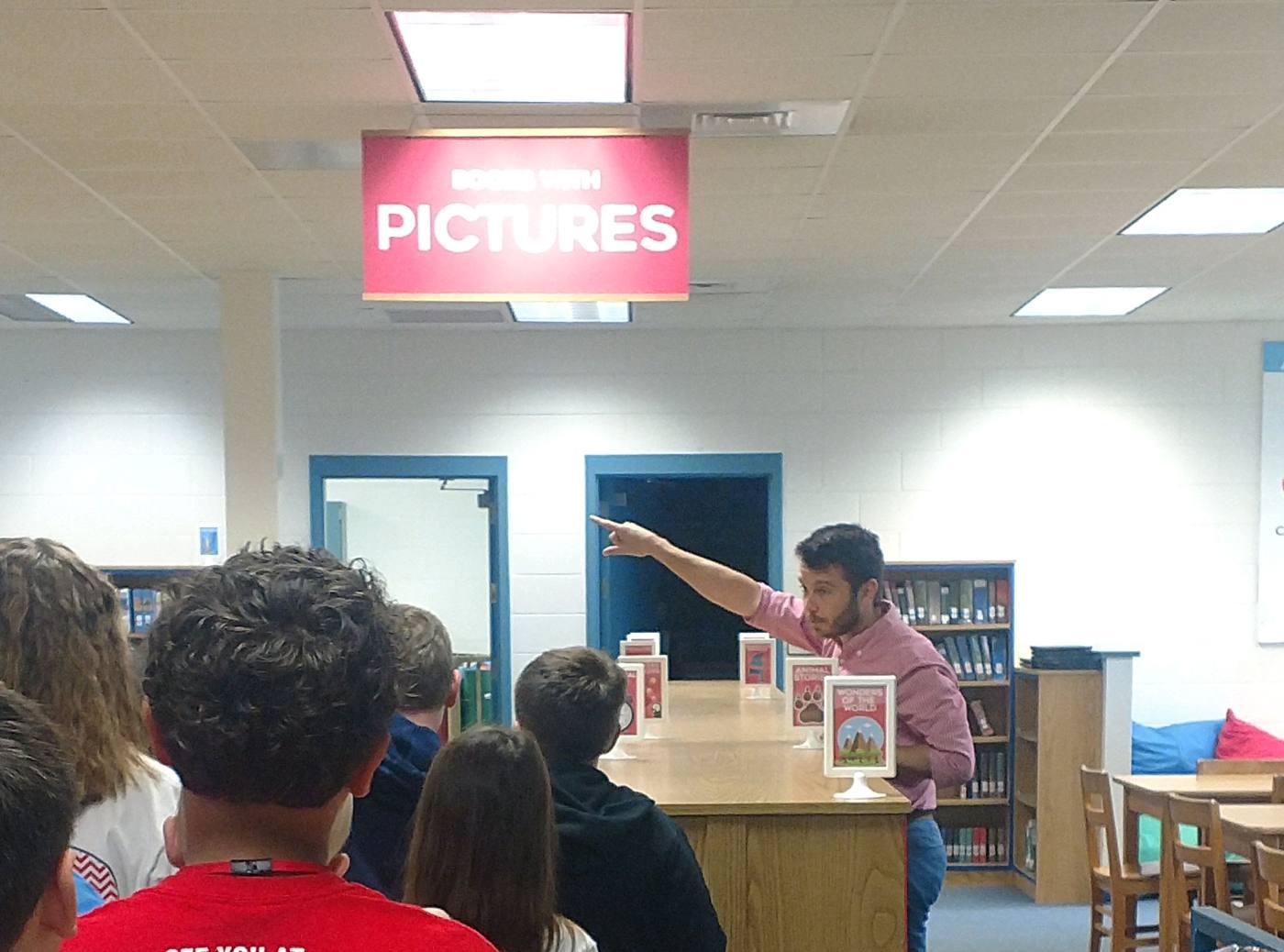 Pointing out the sections to a class gathered under the red Books With Pictures banner.
