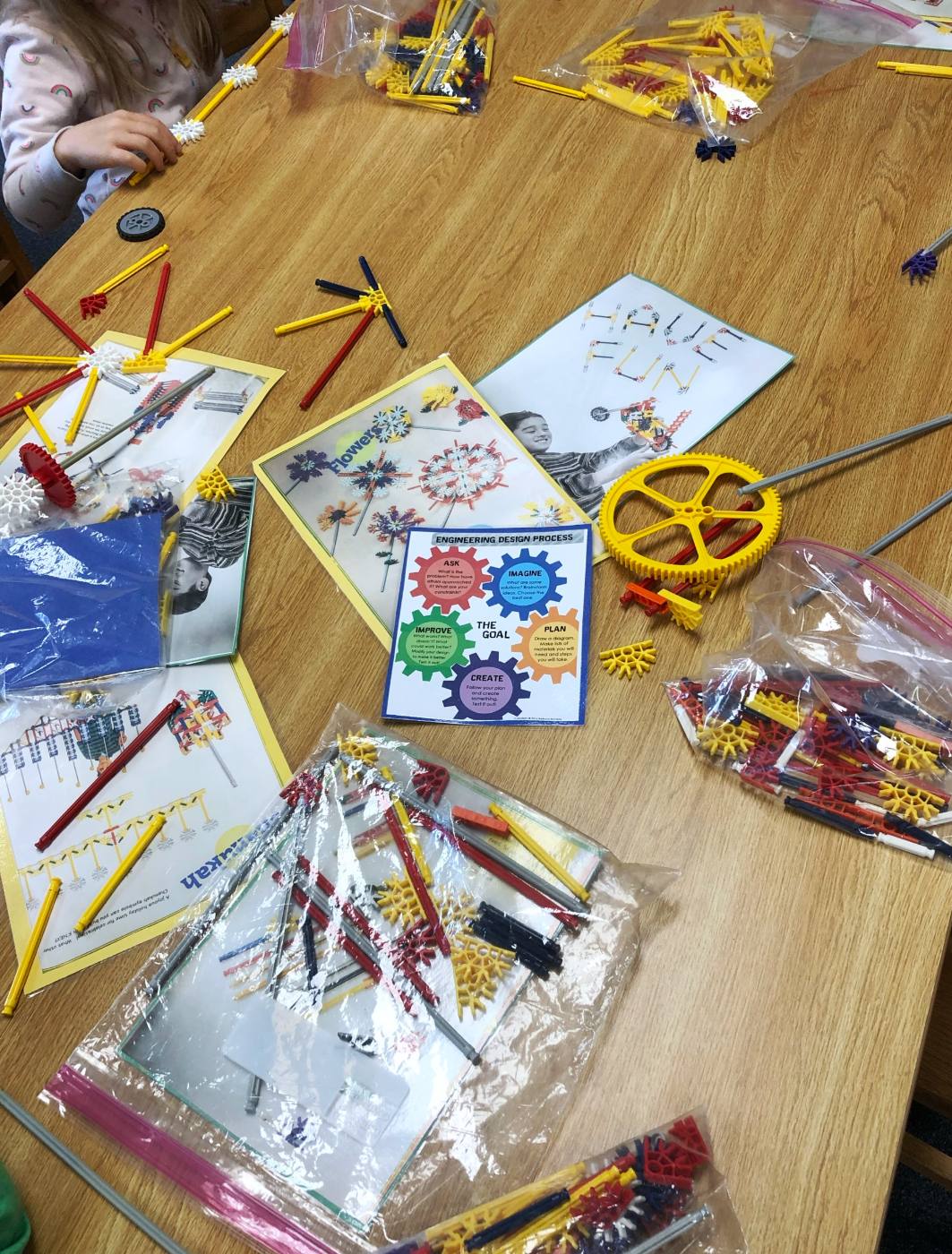 K’NEX pieces in bags and build cards spread across a table around an Engineering Design Process card: Ask, Imagine, Plan, Create, Improve.