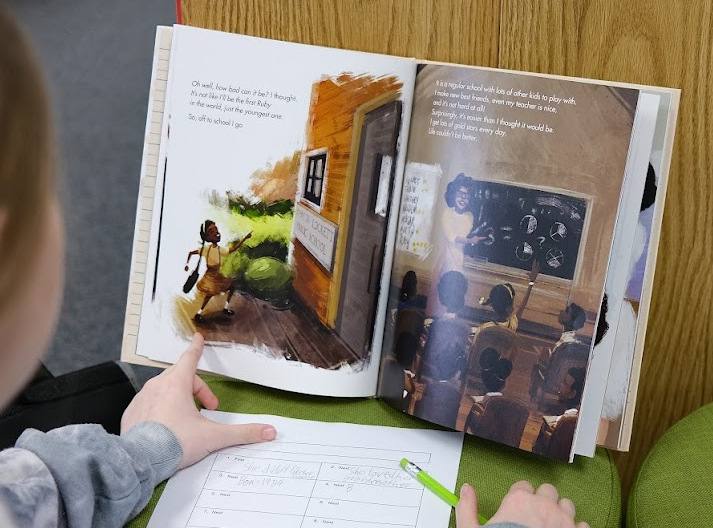 A student reads an open picture book about Ruby Bridges and fills in a graphic organizer on the desk.