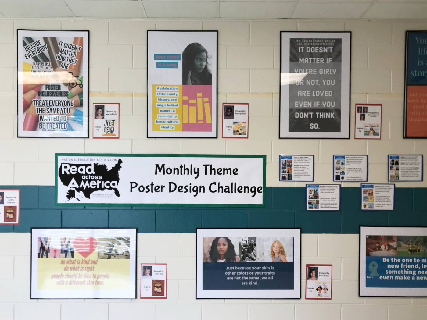 The finished Read Across America wall: student posters in black frames, each with a card naming its designer and the book that inspired it, around a poster-challenge banner with theme cards beside it.